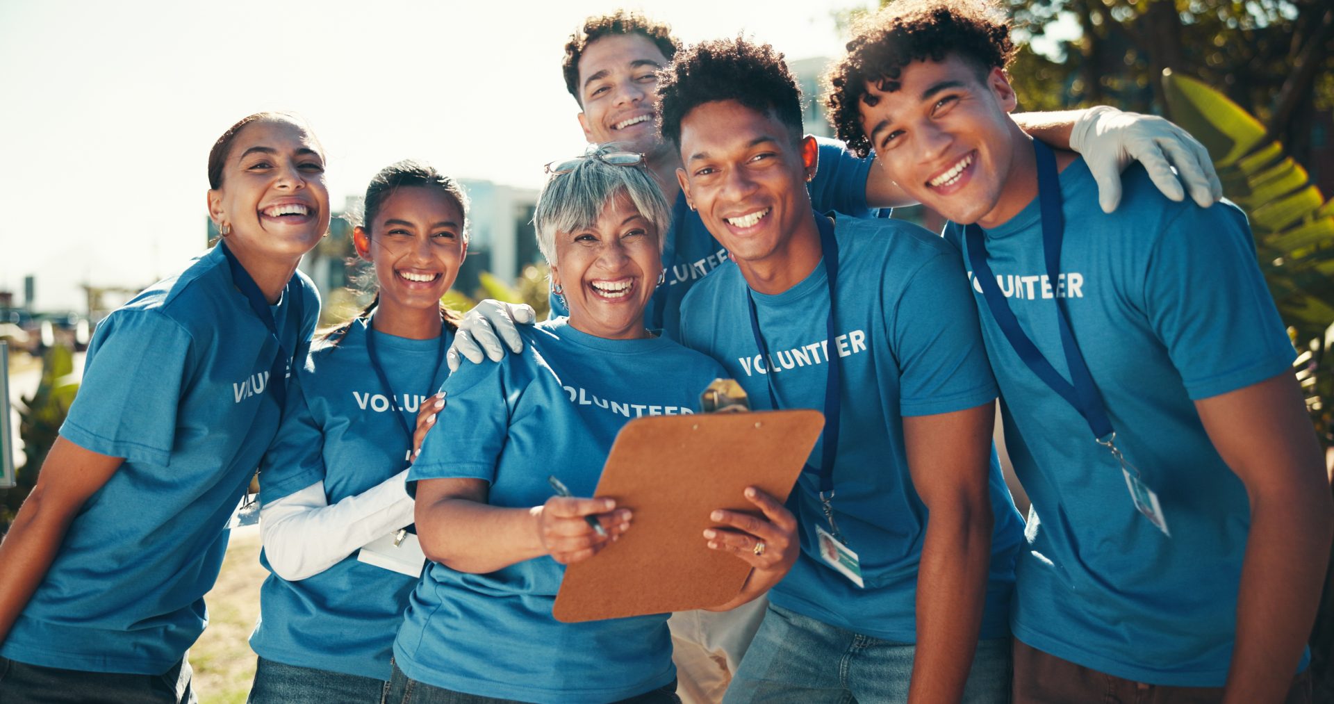 Portrait, happy and group with clipboard, volunteers and joy for collaboration, charity and fundraiser. Outdoor, hug and mature woman with team, smile and good news for community service and USA.